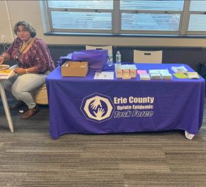 Woman sits at a table with Erie County Opiate Epidemic Task Force materials, including brochures and supplies.